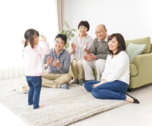 Keluarga jepang yang terdiri dari kakek, nenek,ayah, ibu dan anak di dalam sebuah ruangan. Anak berdiri menghadap ke arah keluarga yang sedang duduk. Kakek dan nenek duduk di atas sofa, ayah dan ibu duduk di atas karpet.