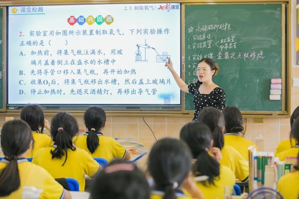 seorang guru yang sedang mengajar di dalam kelas bersama dengan murid-murid.