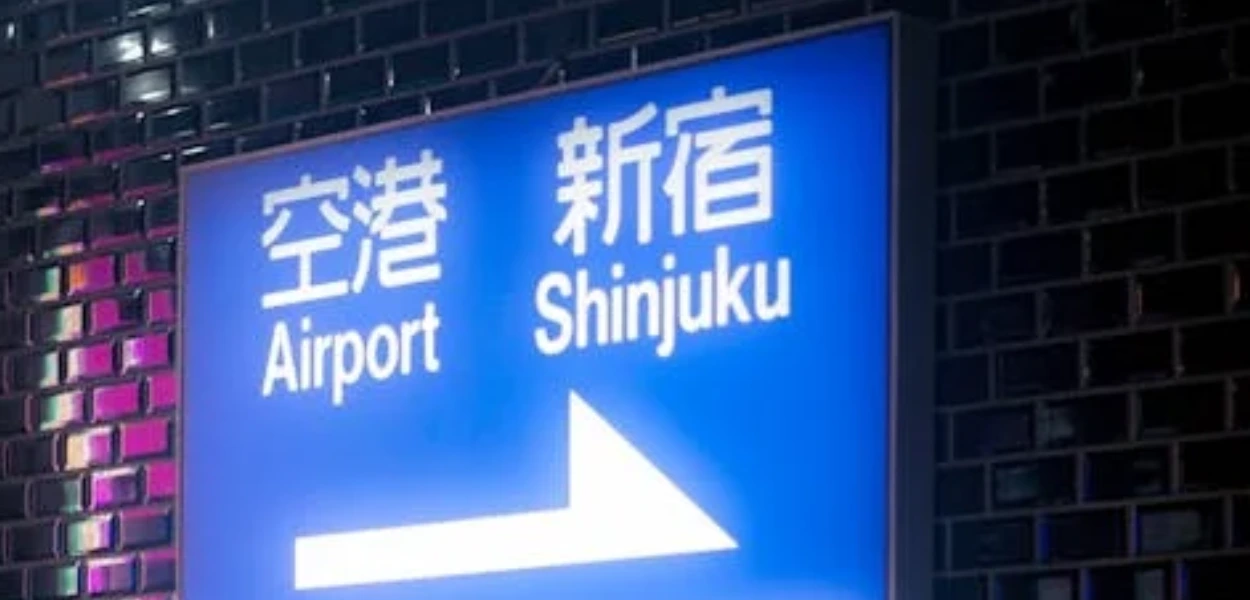 gambar plank petunjuk arah berwarna biru neon bertuliskan airport dan shinjuku serta huruf kanji nya