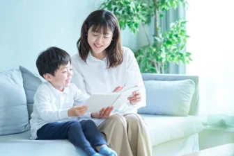 Gambar ibu dan anak yang duduk di atas sofa sambil membaca sebuah buku.